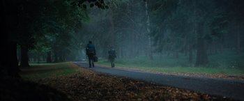 Movie still from “In the Earth” (2021), directed by Ben Wheatley – A couple of people walking down a road in the woods; Extreme Wide shot, Low angle