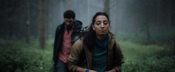 Movie still from “In the Earth” (2021), directed by Ben Wheatley – A man and a woman walking through the woods; Medium shot, Low angle