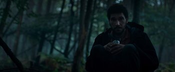 Movie still from “In the Earth” (2021), directed by Ben Wheatley – A man holding a cell phone while standing in the woods; Medium shot, Low angle