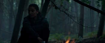 Movie still from “In the Earth” (2021), directed by Ben Wheatley – A woman sitting in the woods next to a fire; Medium shot, Low angle