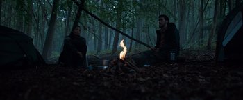 Movie still from “In the Earth” (2021), directed by Ben Wheatley – A man and a woman sitting in front of a campfire; Wide shot, Low angle