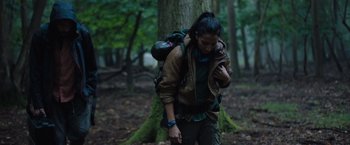 Movie still from “In the Earth” (2021), directed by Ben Wheatley – A woman with a backpack walking in the woods; Medium shot, Low angle