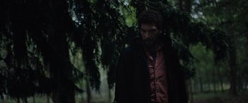 Movie still from “In the Earth” (2021), directed by Ben Wheatley – A man standing in the woods wearing a black jacket; Medium shot, Low angle