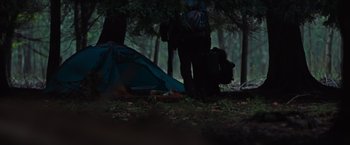 Movie still from “In the Earth” (2021), directed by Ben Wheatley – A man standing next to a tent in the woods; Wide shot, High angle