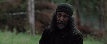 Movie still from “In the Earth” (2021), directed by Ben Wheatley – A man with long hair wearing a hat and a jacket; Close Up shot, Over the shoulder angle