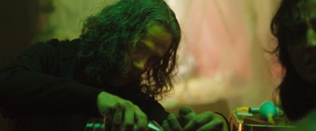 Movie still from “In the Earth” (2021), directed by Ben Wheatley – A person with long hair is holding a green object; Close Up shot, Low angle