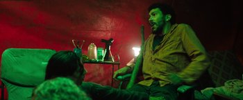 Movie still from “In the Earth” (2021), directed by Ben Wheatley – A man sitting on a chair in a green room; Medium shot, High angle