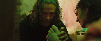 Movie still from “In the Earth” (2021), directed by Ben Wheatley – A man with long green hair is holding a foot; Close Up shot, Low angle