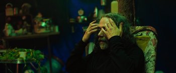 Movie still from “In the Earth” (2021), directed by Ben Wheatley – A man with long grey hair and a beard is holding his hands to his face; Close Up shot, Low angle