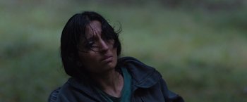 Movie still from “In the Earth” (2021), directed by Ben Wheatley – A person with long hair and a jacket on; Close Up shot, High angle