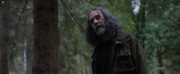 Movie still from “In the Earth” (2021), directed by Ben Wheatley – A man with long hair standing in the woods; Close Up shot, Low angle