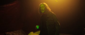 Movie still from “In the Earth” (2021), directed by Ben Wheatley – A man with long curly hair is holding a cup; Medium shot, Over the shoulder angle