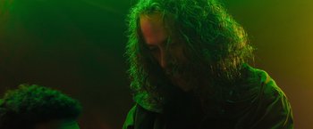 Movie still from “In the Earth” (2021), directed by Ben Wheatley – A man with long green hair is looking down at his face; Close Up shot, Low angle