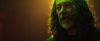 Movie still from “In the Earth” (2021), directed by Ben Wheatley – A man with long hair and a beard is smiling for the camera; Close Up shot, Low angle