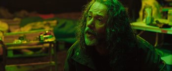 Movie still from “In the Earth” (2021), directed by Ben Wheatley – A man with long hair and a beard is sitting in a dark room; Close Up shot, Over the shoulder angle