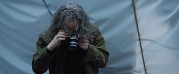 Movie still from “In the Earth” (2021), directed by Ben Wheatley – A man with a long gray hair taking a picture with a camera; Close Up shot, Low angle