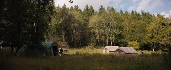 Movie still from “In the Earth” (2021), directed by Ben Wheatley – Some tents in a field with trees in the background; Extreme Wide shot, High angle