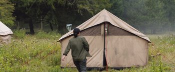 Movie still from “In the Earth” (2021), directed by Ben Wheatley – A person walking in front of a tent in a field; Wide shot, Low angle