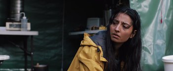 Movie still from “In the Earth” (2021), directed by Ben Wheatley – A woman in a yellow jacket looking at the camera; Close Up shot, Over the shoulder angle