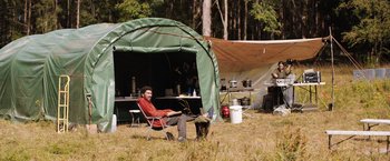 Movie still from “In the Earth” (2021), directed by Ben Wheatley – A man sitting in a chair in the grass; Wide shot, Low angle