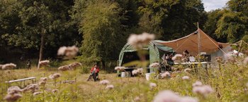 Movie still from “In the Earth” (2021), directed by Ben Wheatley – A man sitting in a field next to a green tent; Extreme Wide shot, Low angle