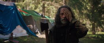 Movie still from “In the Earth” (2021), directed by Ben Wheatley – A man with long grey hair holding an axe in his hand; Medium shot, Over the shoulder angle