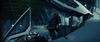 Movie still from “Independence Day: Resurgence” (2016), directed by Roland Emmerich – A woman standing in front of a tv in a room; Medium shot, Low angle