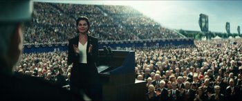 Movie still from “Independence Day: Resurgence” (2016), directed by Roland Emmerich – A woman standing at a podium in front of a crowd of people; Medium shot, Over the shoulder angle