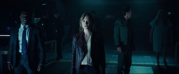 Movie still from “Independence Day: Resurgence” (2016), directed by Roland Emmerich – A woman wearing a leather jacket standing in a dark room; Medium shot, Over the shoulder angle