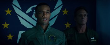 Movie still from “Independence Day: Resurgence” (2016), directed by Roland Emmerich – A man standing next to another man in front of a flag; Close Up shot, Low angle