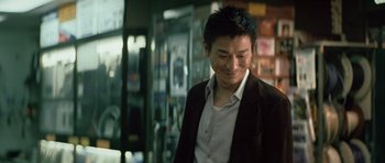 Movie still from “Infernal Affairs” (2002), directed by Alan Mak – A man in a suit and tie standing in front of a window; Medium shot, Over the shoulder angle