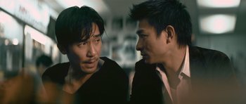 Movie still from “Infernal Affairs” (2002), directed by Alan Mak – Two asian men talking to each other in a dark room; Close Up shot, Over the shoulder angle