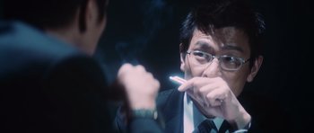 Movie still from “Infernal Affairs” (2002), directed by Alan Mak – A man smoking a cigarette in front of another man; Close Up shot, Low angle