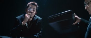 Movie still from “Infernal Affairs” (2002), directed by Alan Mak – A man in a black suit holding a wine glass; Medium shot, Low angle