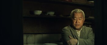 Movie still from “Infernal Affairs” (2002), directed by Alan Mak – A man sitting in front of a table with bowls on it; Close Up shot, Low angle