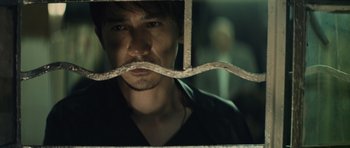 Movie still from “Infernal Affairs” (2002), directed by Alan Mak – A person behind a metal fence; Close Up shot, Over the shoulder angle