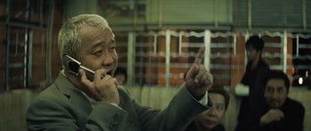 Movie still from “Infernal Affairs” (2002), directed by Alan Mak – An older man talking on a cell phone; Medium shot, Low angle