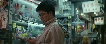Movie still from “Infernal Affairs” (2002), directed by Alan Mak – A man is looking at his cell phone in a store; Medium shot, Low angle