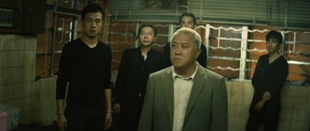 Movie still from “Infernal Affairs” (2002), directed by Alan Mak – A group of men standing next to each other in front of a brick wall; Medium shot, Low angle
