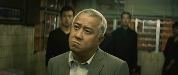 Movie still from “Infernal Affairs” (2002), directed by Alan Mak – A man in a gray suit is looking at the camera; Close Up shot, Low angle
