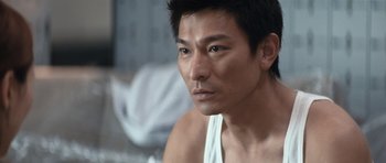 Movie still from “Infernal Affairs” (2002), directed by Alan Mak – A person sitting on a bed; Close Up shot, Over the shoulder angle