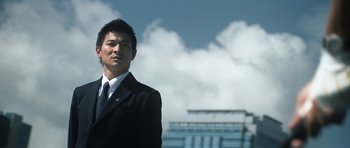 Movie still from “Infernal Affairs” (2002), directed by Alan Mak – A man wearing a suit and tie standing in front of a building; Medium shot, Low angle
