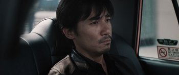 Movie still from “Infernal Affairs” (2002), directed by Alan Mak – A person sitting in a car; Close Up shot, Low angle