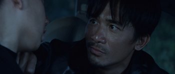 Movie still from “Infernal Affairs” (2002), directed by Alan Mak – A person in a car looking at the camera; Close Up shot, Over the shoulder angle