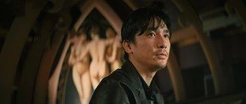 Movie still from “Infernal Affairs” (2002), directed by Alan Mak – A man in a black shirt is in front of some statues; Close Up shot, Low angle