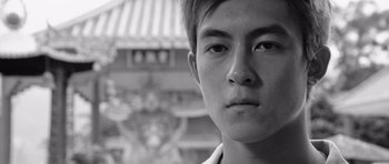 Movie still from “Infernal Affairs” (2002), directed by Alan Mak – Black and white photograph of a young man in front of a temple; Close Up shot, Low angle