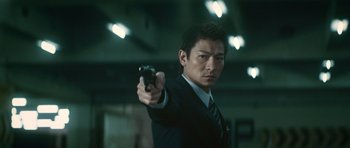 Movie still from “Infernal Affairs” (2002), directed by Alan Mak – A man in a suit and tie holding a gun; Close Up shot, Low angle