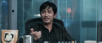 Movie still from “Infernal Affairs” (2002), directed by Alan Mak – A man sitting in a chair holding a remote control; Close Up shot, Over the shoulder angle