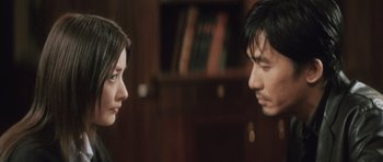 Movie still from “Infernal Affairs” (2002), directed by Alan Mak – A man and a woman face to face in front of a bookshelf; Close Up shot, Over the shoulder angle
