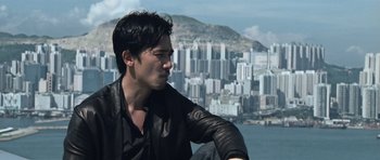 Movie still from “Infernal Affairs” (2002), directed by Alan Mak – A man in a black shirt is looking at a city; Close Up shot, Low angle